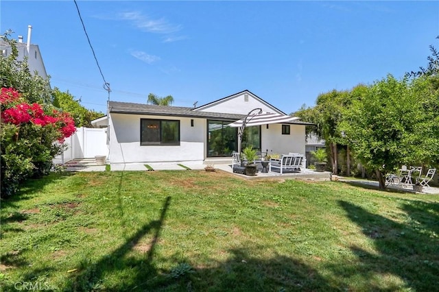 rear view of house with fence, a lawn, a patio, and stucco siding