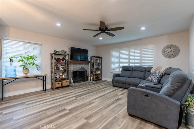 living area featuring baseboards, a fireplace with raised hearth, a ceiling fan, light wood-style flooring, and recessed lighting