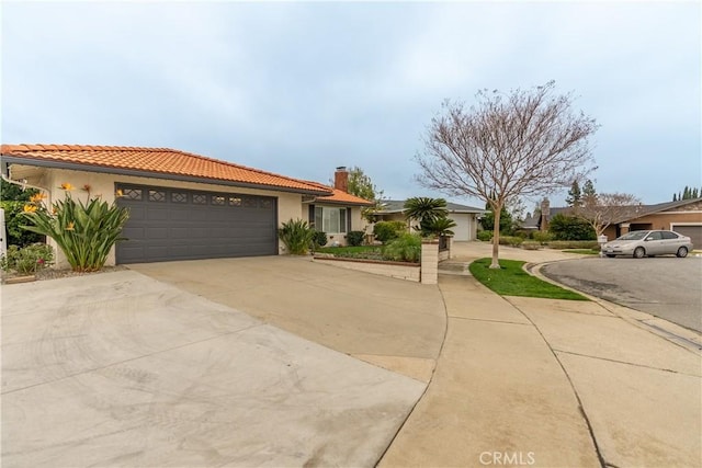 view of front of house with an attached garage, concrete driveway, a tiled roof, stucco siding, and a chimney