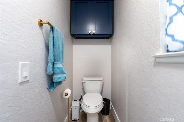 bathroom with toilet, baseboards, wood finished floors, and a textured wall