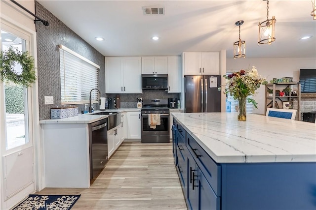 kitchen with stainless steel appliances, a sink, visible vents, white cabinetry, and a center island