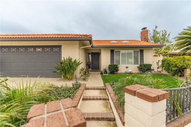 mediterranean / spanish home with a garage, fence, a tiled roof, stucco siding, and a chimney