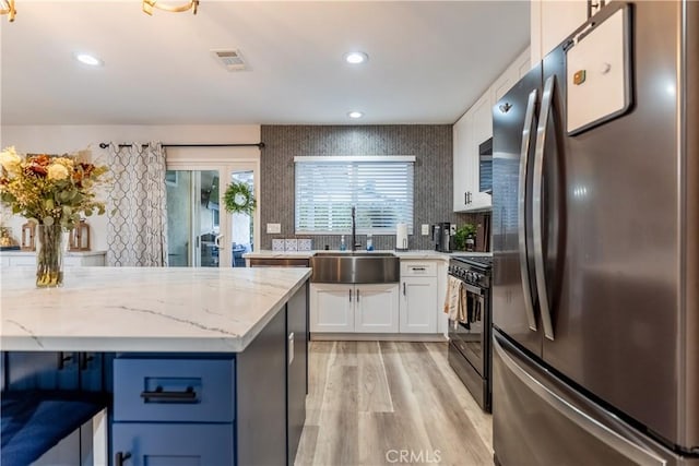 kitchen featuring light stone counters, freestanding refrigerator, gas stove, white cabinetry, and a sink