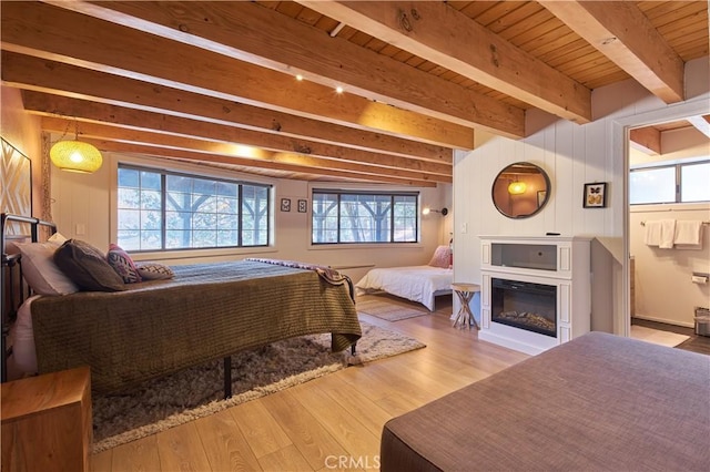 bedroom with a glass covered fireplace, beamed ceiling, wood finished floors, and wood ceiling