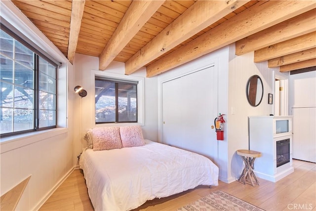 bedroom with a glass covered fireplace, wooden ceiling, beamed ceiling, and light wood finished floors