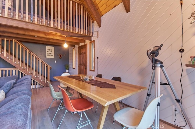 dining space with stairs, beam ceiling, wooden walls, high vaulted ceiling, and hardwood / wood-style flooring