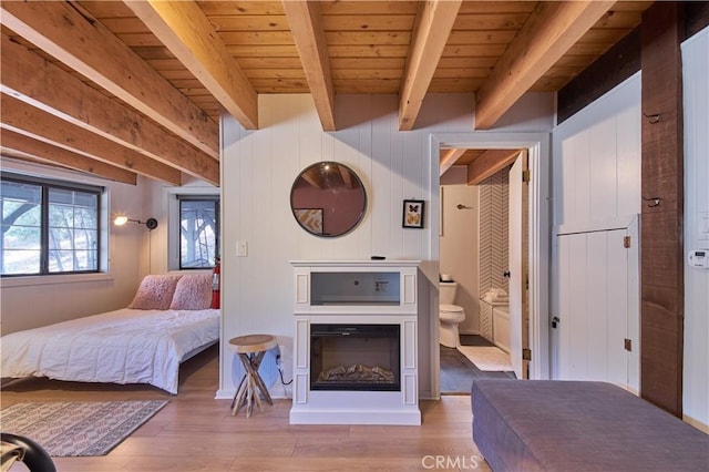 bedroom featuring wooden ceiling, light wood-style flooring, beam ceiling, and a glass covered fireplace