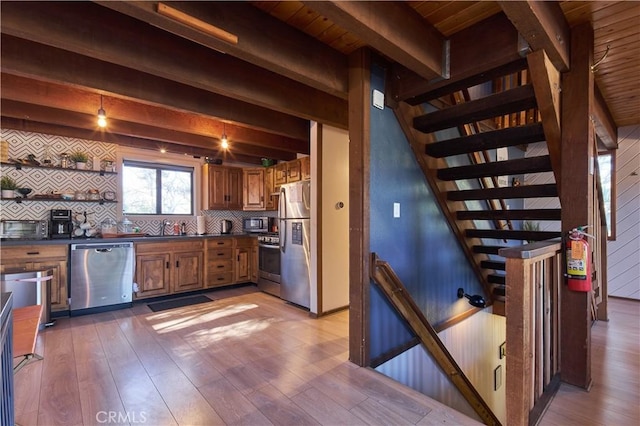 kitchen with brown cabinetry, dark countertops, wood finished floors, stainless steel appliances, and beam ceiling