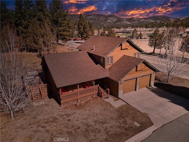 chalet / cabin featuring driveway, a garage, stone siding, a mountain view, and a porch