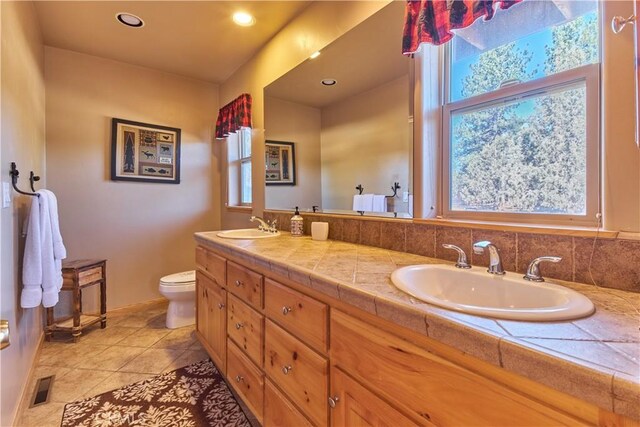 full bath with toilet, double vanity, visible vents, and a sink