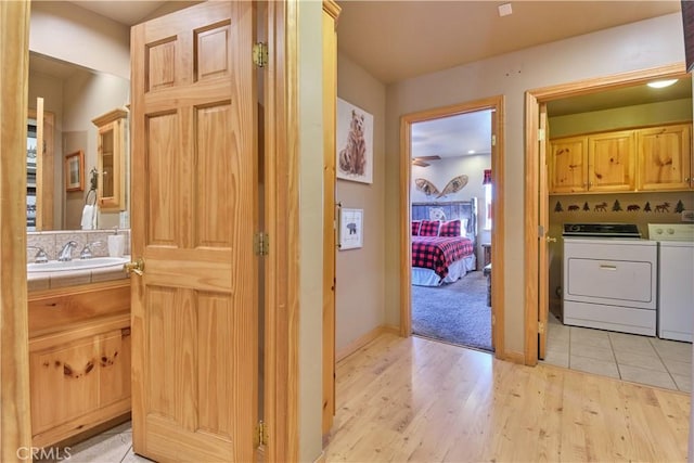 hallway featuring a sink, washing machine and clothes dryer, and light wood-style flooring