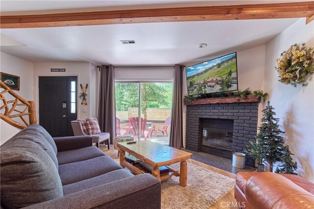 living room featuring a brick fireplace, visible vents, stairway, and wood finished floors