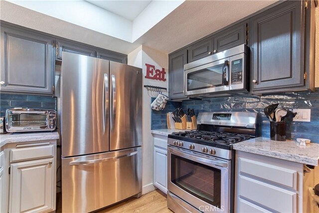 kitchen featuring light stone counters, light wood-style flooring, a toaster, stainless steel appliances, and decorative backsplash