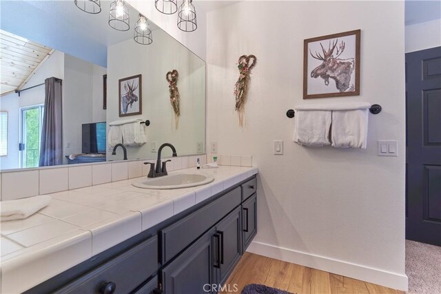 bathroom featuring vaulted ceiling, wood finished floors, vanity, and baseboards