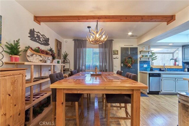 dining area featuring light wood-style flooring, beam ceiling, and an inviting chandelier