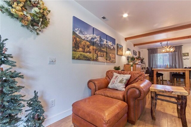 living area with beam ceiling, a notable chandelier, visible vents, wood finished floors, and baseboards