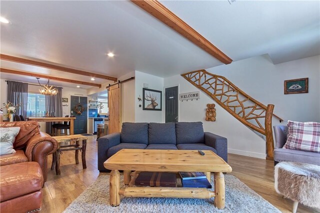 living room featuring stairs, a barn door, light wood-type flooring, and beam ceiling