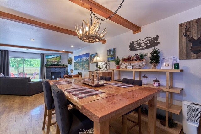 dining room featuring a notable chandelier, recessed lighting, light wood-style floors, a brick fireplace, and beamed ceiling