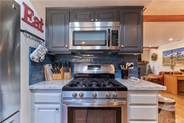 kitchen featuring light stone counters, stainless steel appliances, a fireplace, wood finished floors, and decorative backsplash