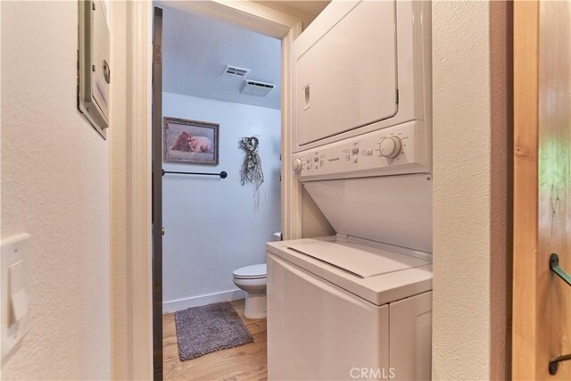 washroom with laundry area, stacked washer and dryer, visible vents, baseboards, and light wood-style floors