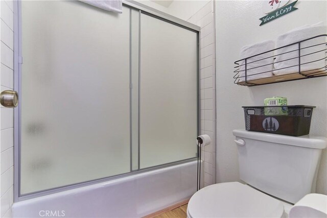 bathroom featuring enclosed tub / shower combo, toilet, and wood finished floors