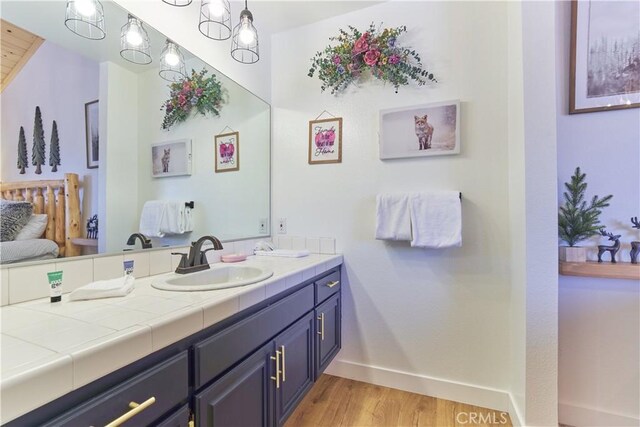 ensuite bathroom with baseboards, ensuite bathroom, wood finished floors, and vanity