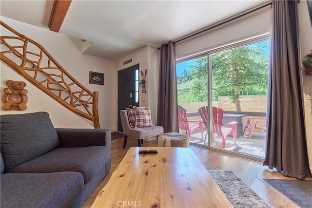 living area with beam ceiling, stairway, and wood finished floors