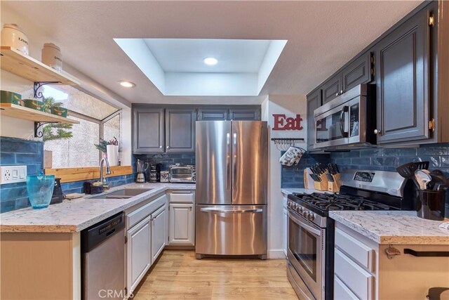 kitchen with light wood-style flooring, a tray ceiling, stainless steel appliances, open shelves, and a sink