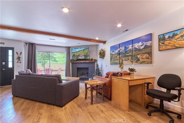 living area with light wood-style floors, a fireplace, visible vents, and beamed ceiling