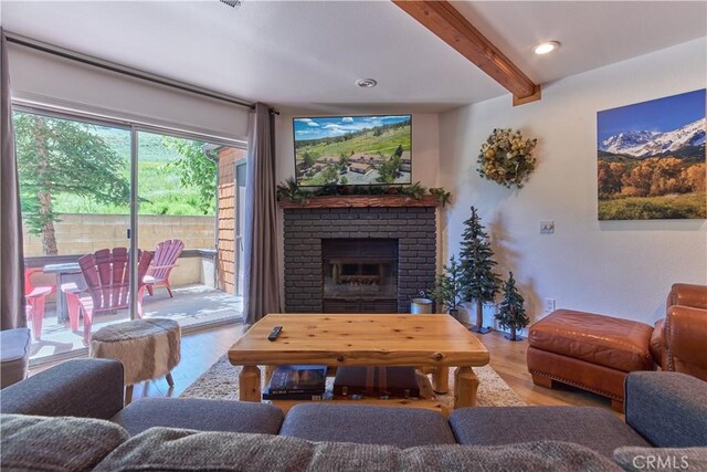 living area featuring a brick fireplace, beam ceiling, recessed lighting, and wood finished floors