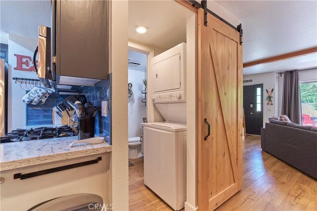 laundry room with stacked washing maching and dryer, a barn door, laundry area, and light wood-style floors