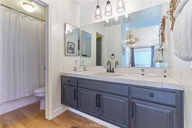 full bath featuring toilet, wood finished floors, an inviting chandelier, shower / bath combination with curtain, and vanity