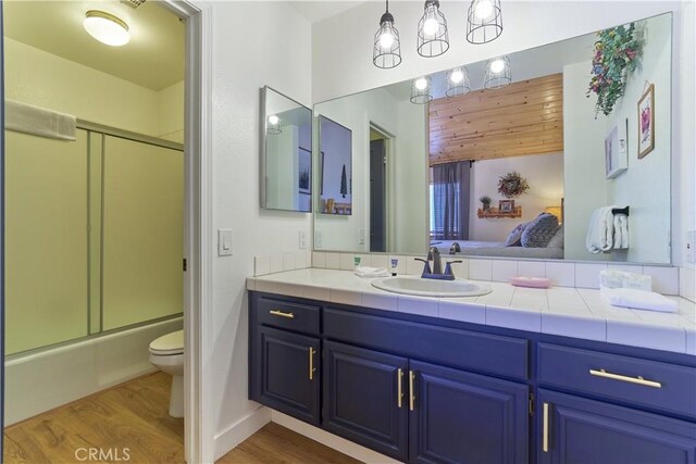 full bathroom featuring connected bathroom, toilet, wood finished floors, vanity, and combined bath / shower with glass door