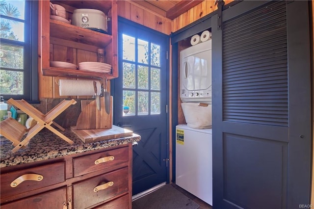 laundry area with laundry area, a barn door, wood walls, and stacked washer / drying machine