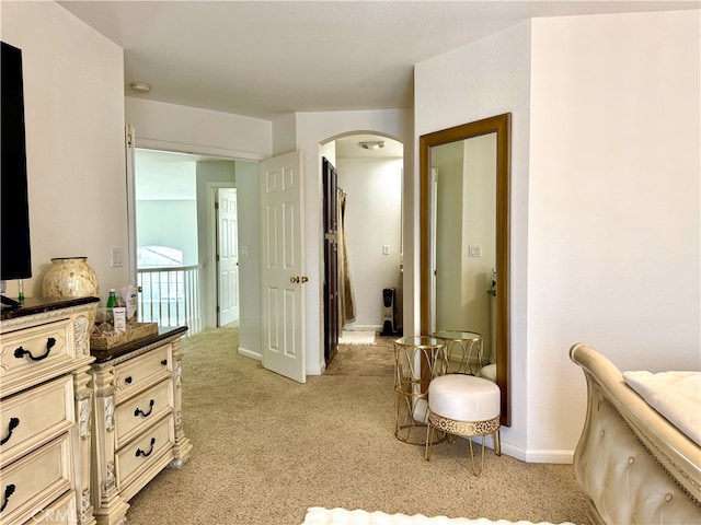 bedroom featuring baseboards, arched walkways, and light colored carpet