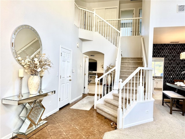 tiled entrance foyer with arched walkways, visible vents, a towering ceiling, baseboards, and stairs