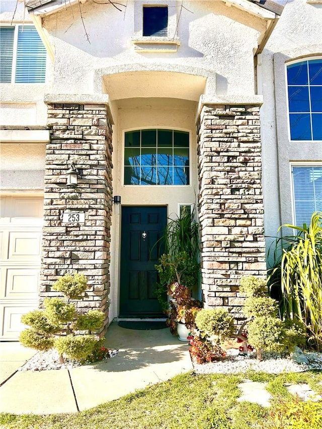 doorway to property featuring stucco siding, stone siding, and a garage