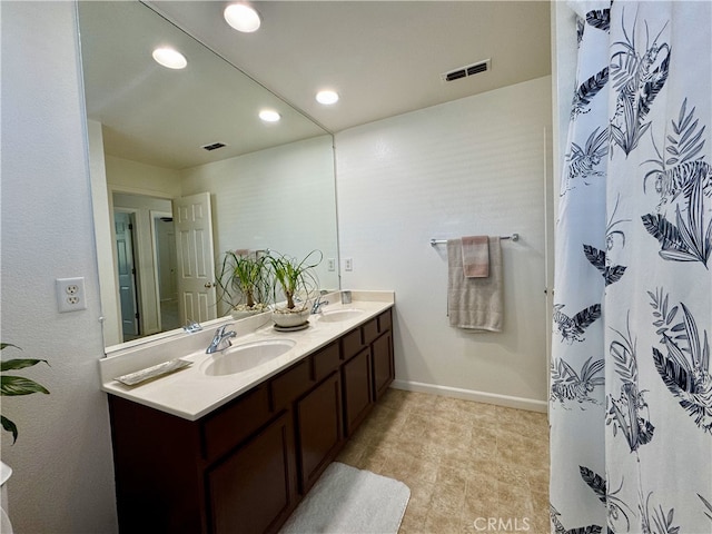 bathroom with double vanity, baseboards, visible vents, and a sink