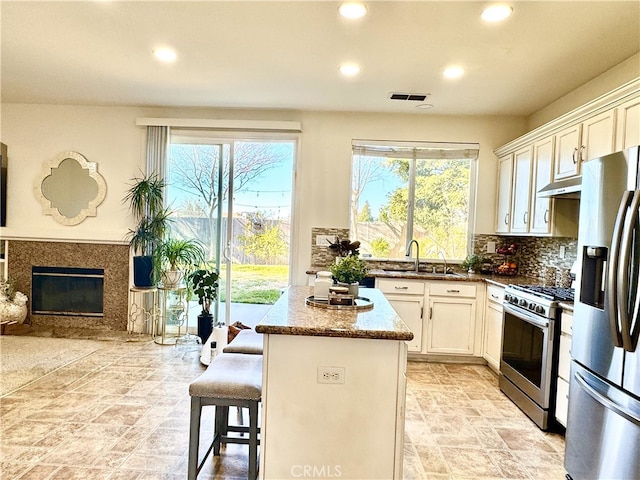 kitchen with visible vents, a kitchen island, stainless steel appliances, under cabinet range hood, and a sink