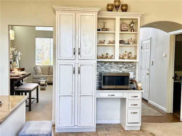 kitchen with arched walkways, open shelves, light stone counters, and stainless steel microwave