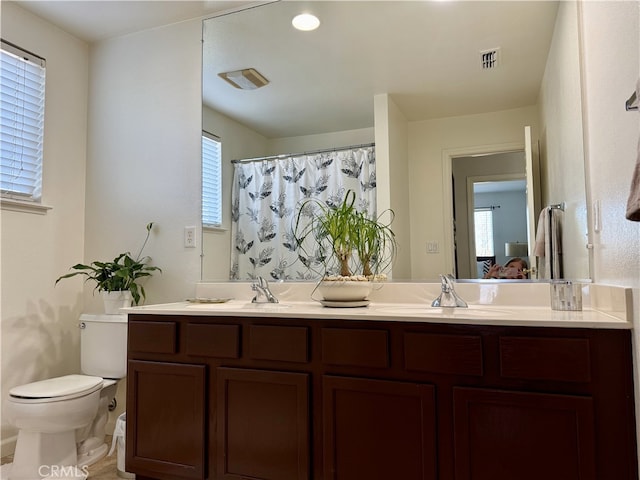 full bath featuring double vanity, visible vents, toilet, a healthy amount of sunlight, and a sink