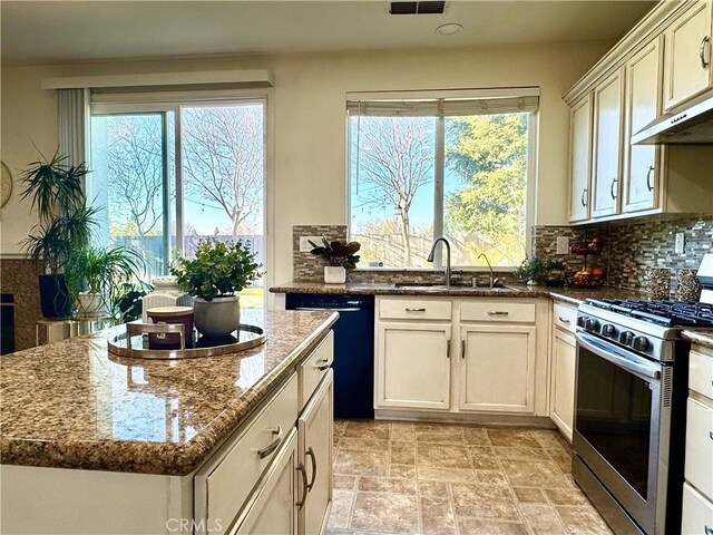 kitchen featuring black dishwasher, tasteful backsplash, a sink, dark stone countertops, and stainless steel gas range oven