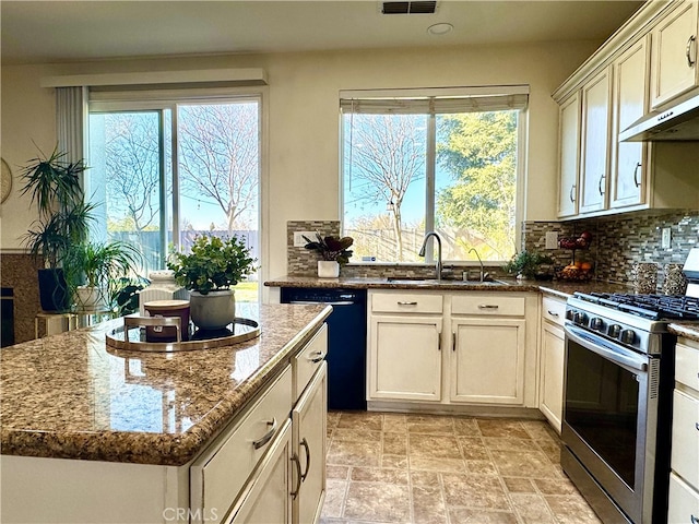kitchen with backsplash, dark stone counters, black dishwasher, stainless steel gas stove, and a sink