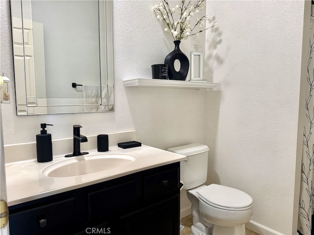 bathroom with toilet, a textured wall, vanity, and baseboards