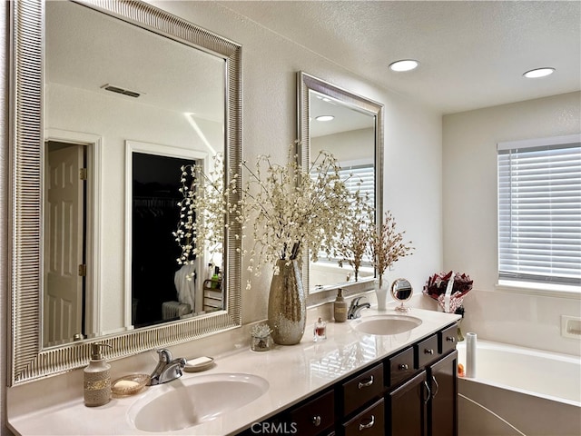 bathroom featuring a garden tub, double vanity, a closet, and a sink