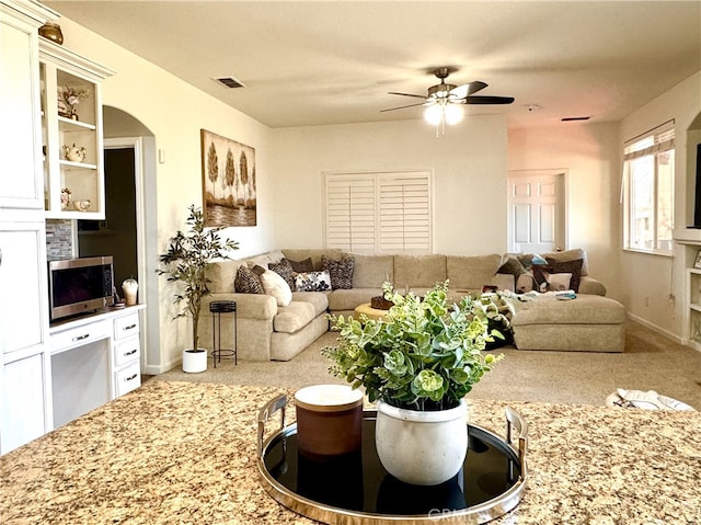 living room featuring visible vents, arched walkways, a ceiling fan, and carpet flooring