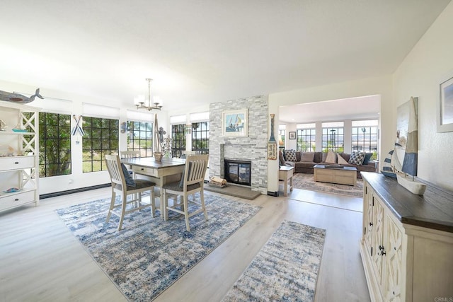 dining room with light wood-type flooring, plenty of natural light, a chandelier, and a stone fireplace