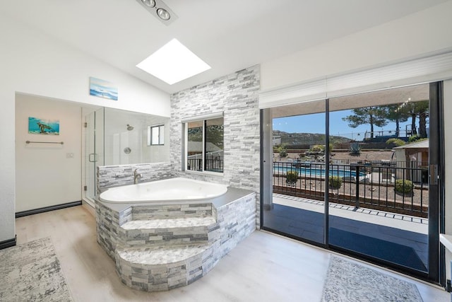 bathroom with lofted ceiling with skylight, a shower stall, a garden tub, and wood finished floors