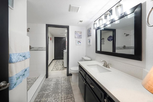 full bath with toilet, visible vents, a tile shower, and vanity