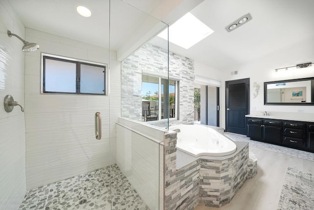 bathroom with a skylight, wood finished floors, a jetted tub, vanity, and a shower stall